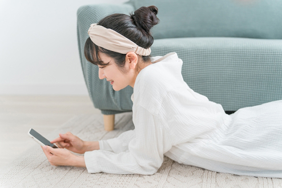 くつろぎながらスマホをいじる女性の写真
